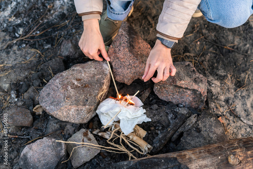 Cropped view of the caucasian woman making campfire while sitting near the rocks at the nature and holding dry sticks