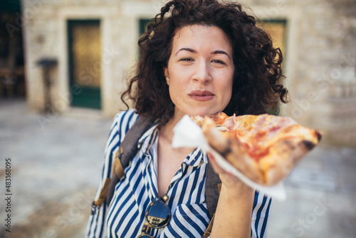 Beautiful young tourist woman eating a slice of pizza outdoor