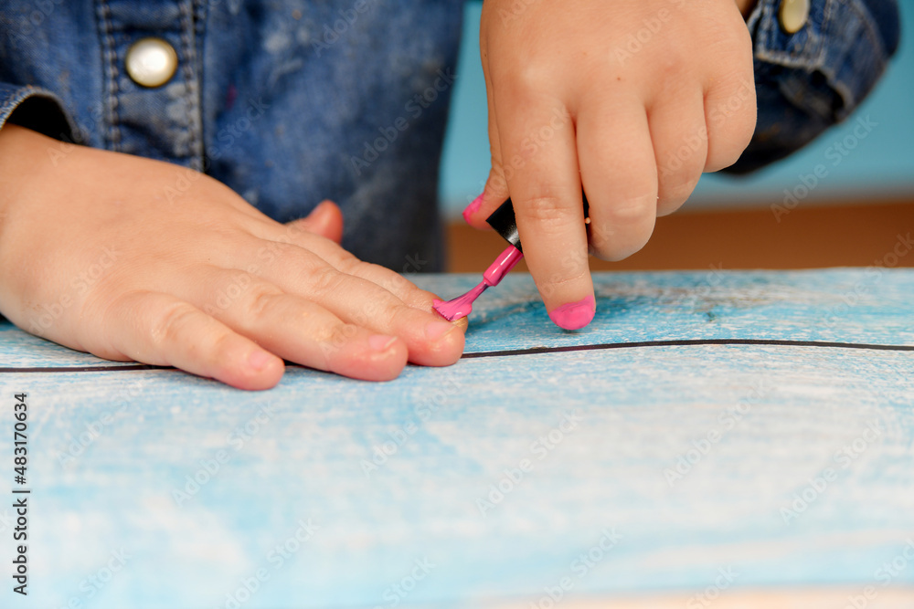 A little girl ineptly paints her nails with varnish from her mother's cosmetics. A little girl ineptly paints her nails with varnish from her mother's cosmetics.