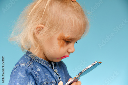 The child looks at himself in the mirror after ineptly used parental makeup. photo