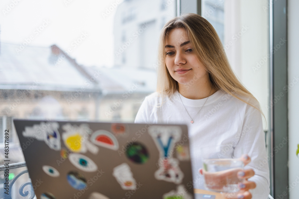 Girl with a glass of water in her hand works on a laptop Girl with a glass of water in her hand works on a laptop