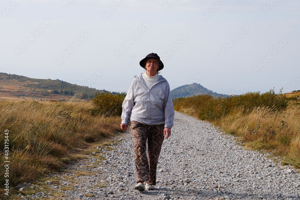 an elderly woman walks along the road against the backdrop of the mountains an elderly woman walks along the road against the backdrop of the mountains