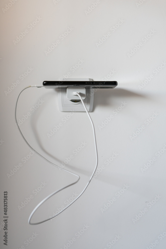 Mobile phone charging battery while on charger against white wall copy space Mobile phone charging battery while on charger against white wall copy space