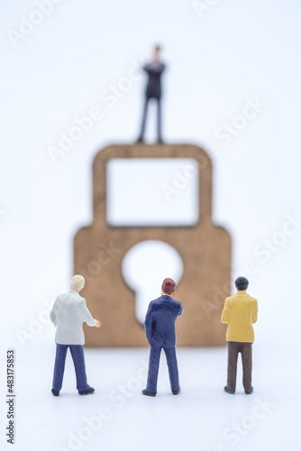 Money and Security Concept. Closeup of group of businessman miniature figure people standing and looking to business man standing on wooden master key lock icon on white background.