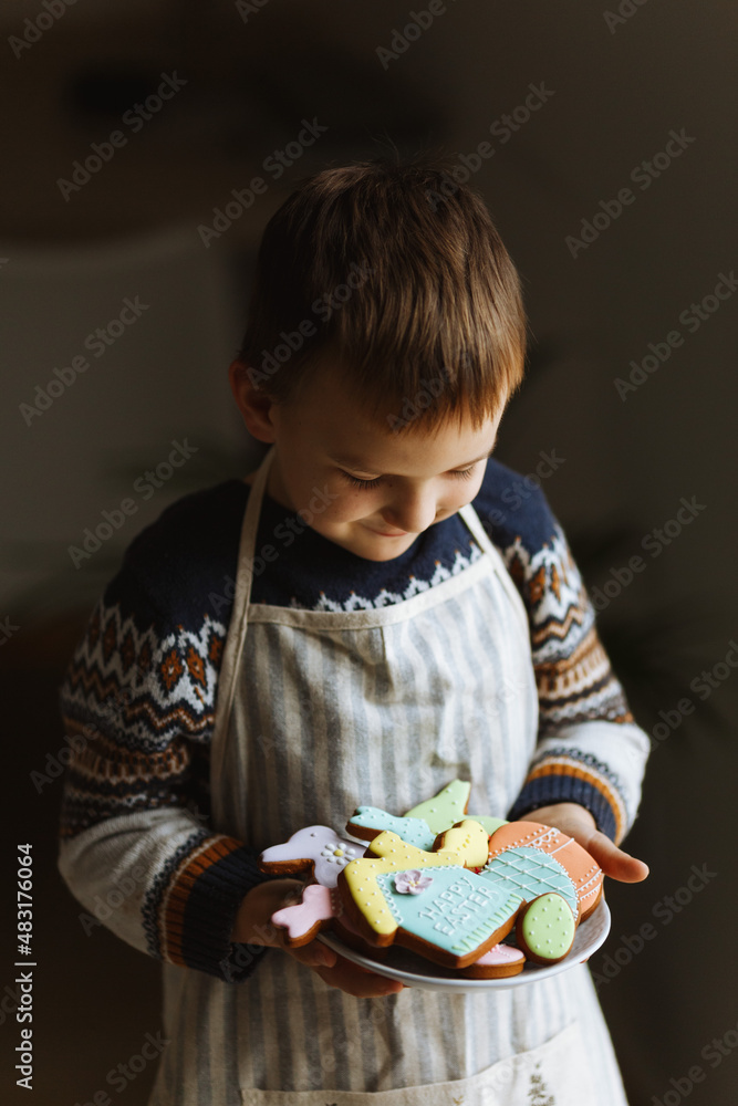 A child in his hands holding a plate with Easter eggs, bunny, chicken and house made from homemade cookies. A child in his hands holding a plate with Easter eggs, bunny, chicken and house made from homemade cookies.