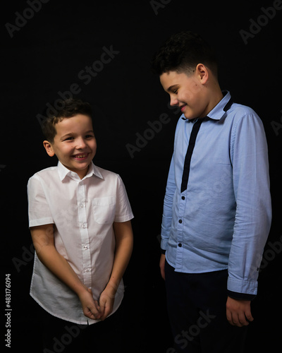 Two boys on a black background are brothers. they look at each other.Senior and junior.A child's smile