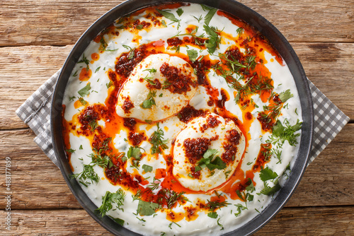 Turkish eggs with garlic yogurt and spicy butter dressing close-up in a plate on the table. horizontal top view from above photo