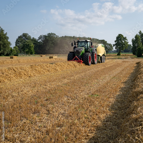 Strohernte - schlagkr  ftige Landtechnik im Ernteeinsatz.  Gr  ner Traktor mit angeh  ngt Presse beim pressen von Strohballen.