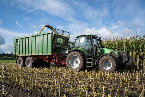 Maisernte -  Traktor mit Erntewagen f  hrt neben dem H  cksler her  um das Erntegut zu laden.