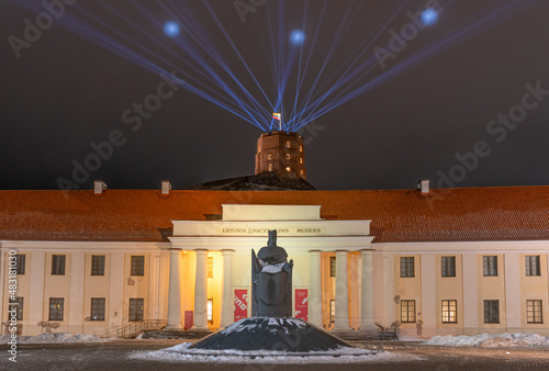 Vilnius Light Festival. National Museum of Lithuania and Gediminas statue and tower or castle in winter with snow and laser lights in the sky photo