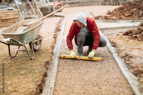 construction worker installing and laying pavement stones on terrace, road or sidewalk. Worker using pavement slabs and level to build stone sidewalk