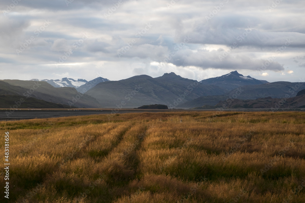Paisaje con una bonita luz de atardecer, campo sembrado, montañas, nieva y nubes en Islandia.