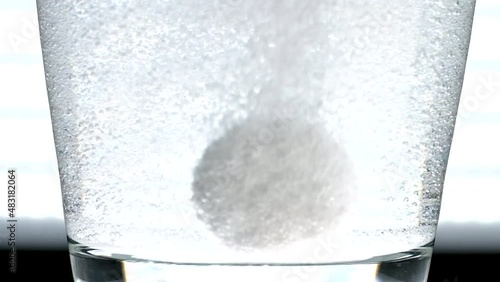 Antacid tablets dissolving in a backlit glass of water before floating up out of frame.  Dense bubbles stick to the inside of the glass, macro view of carbonation release from otc medication. photo