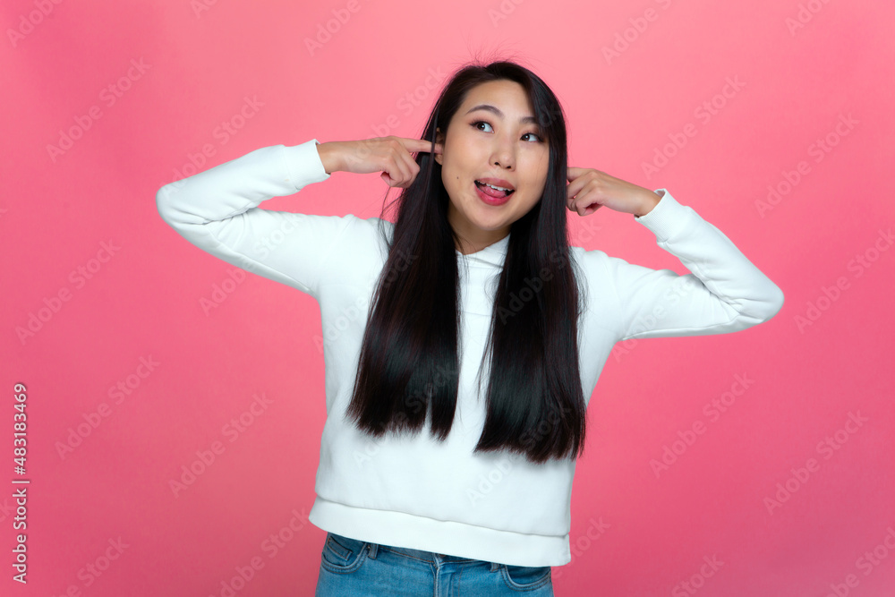 Funny young asian girl covering ears with fingers, refusing to listen, grimacing, fooling on pink studio background Funny young asian girl covering ears with fingers, refusing to listen, grimacing, fooling on pink studio background