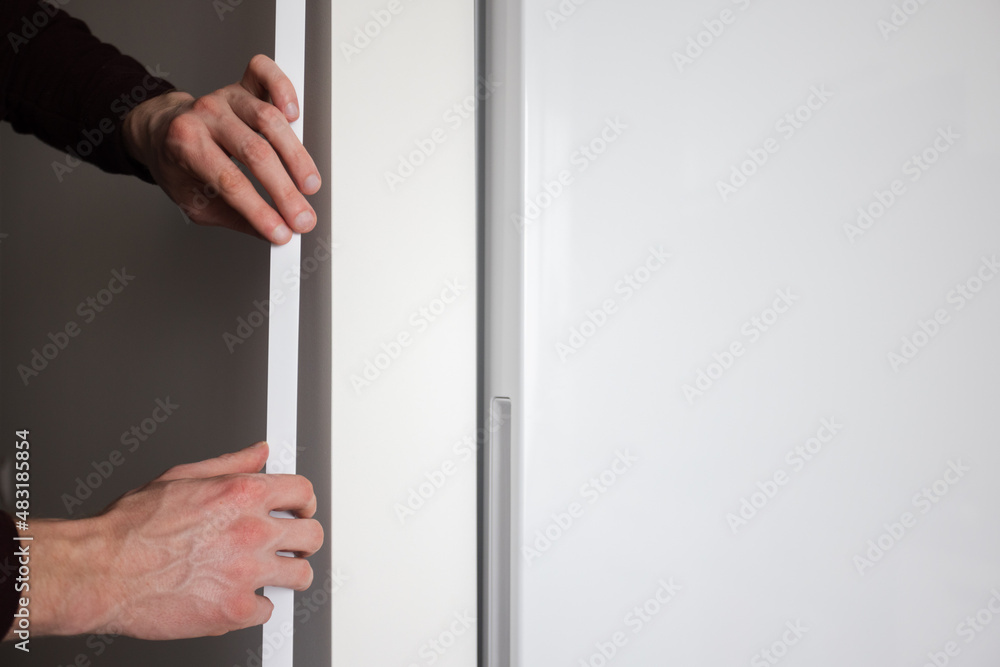 Mans hands installing protective decorative corner on the wall in apartment. Mans hands installing protective decorative corner on the wall in apartment.