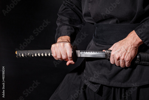 The samurai holding a Japanese katana sword. Photo of a warrior dressed in black clothes in low key with selective focus