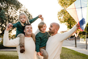 Gay fathers and children playing together at city park - LGBT family love concept - Main focus on left man face