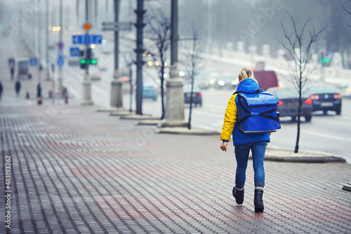 Delivery person with thermal backpack deliver fast food orders to customers in hazy day. Delivery boy walking with thermal bag on winter city street. Man of delivery service in deliver an order