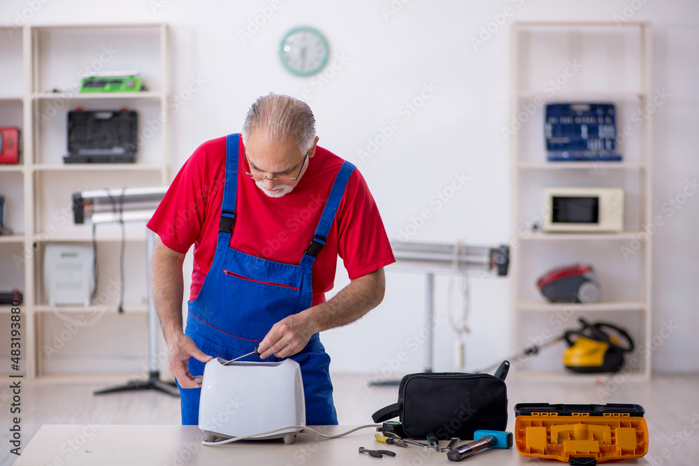 Old repairman repairing toaster at workshop Old repairman repairing toaster at workshop