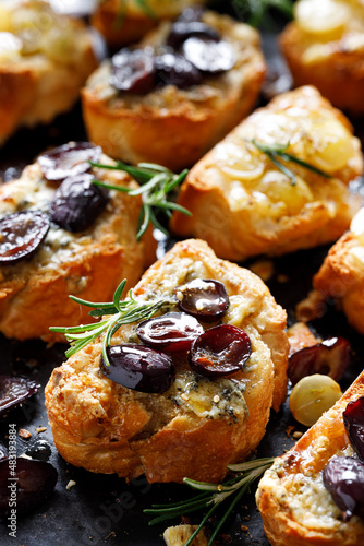 Crostini of sliced baguette with the addition of grapes, seasoned with herbs and honey on a dark background, close-up view.