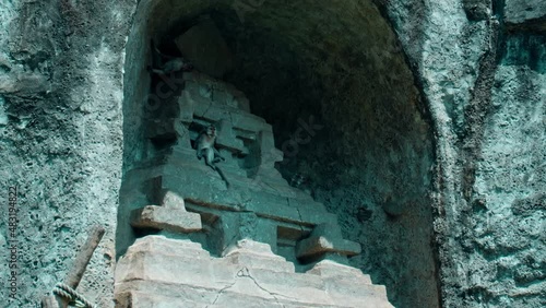 monkey sits in an old stone town at a stone gate and eats fruit