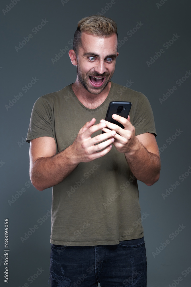 Excited young man receiving winning news on his phone, celebrating and feeling victorious, jumping for joy, studio image Excited young man receiving winning news on his phone, celebrating and feeling victorious, jumping for joy, studio image