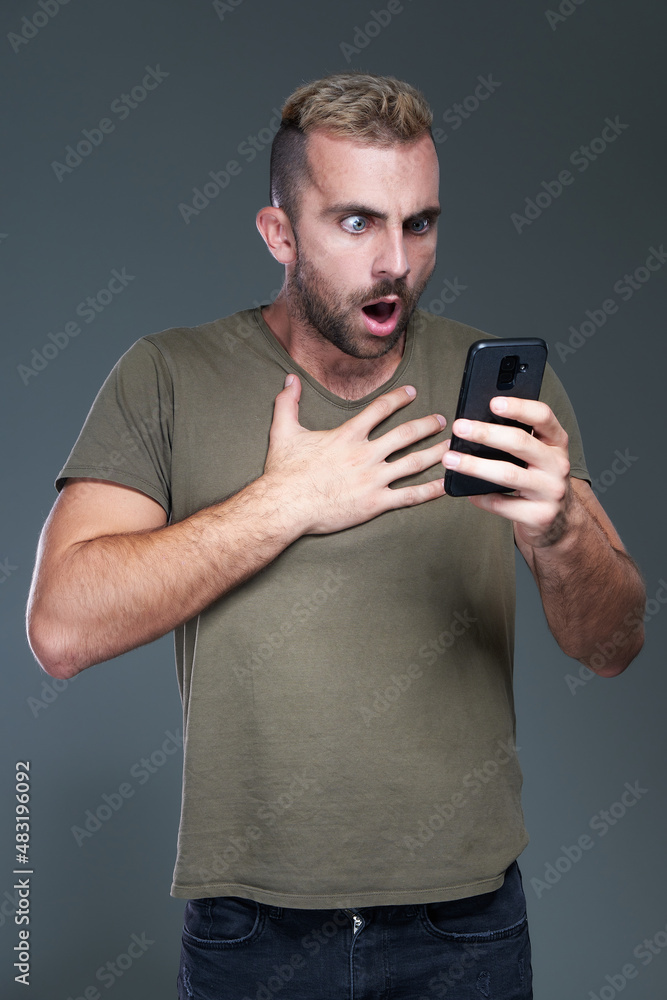 Bad news on the phone: Shocked and frightened young caucasian man checking his phone, terrified with its content Bad news on the phone: Shocked and frightened young caucasian man checking his phone, terrified with its content