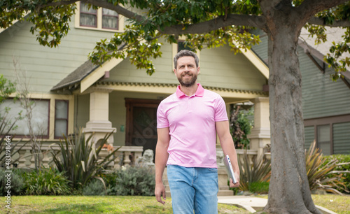 cheerful bearded man real estate agent selling or renting house walk with computer, neighborhood