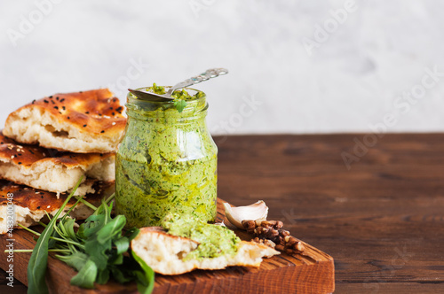 Green pesto sauce in a jar on a wooden board.