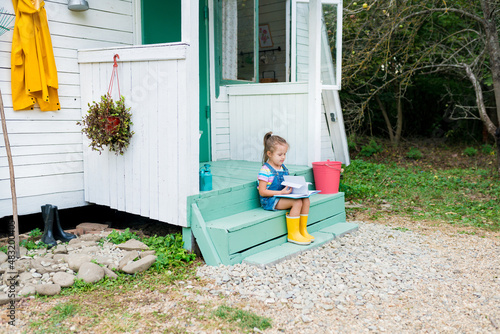 Cute child girl sitting on steps and reading book on backyard. Toddler developmet  independent reading outside. countryside photo