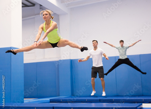 Young athletic woman practicing side split in jump on trampoline in sports center..
