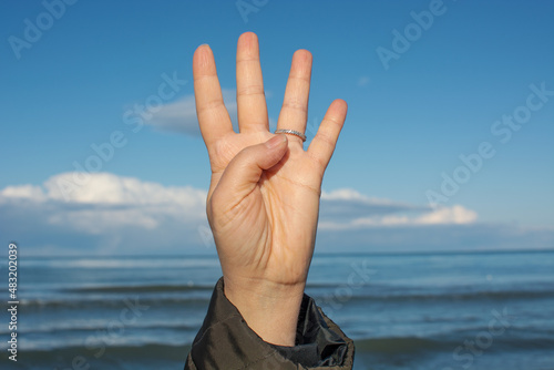 Female hand showing number four, isolated blue sky and white cloud background.