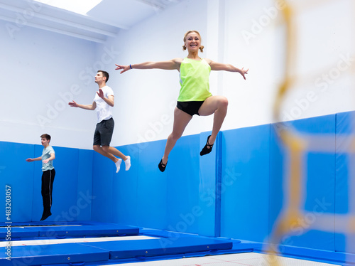 Smiling female gymnast jumping and bouncing on trampoline during workout in modern fitness center