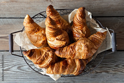 Fresh crispy french croissants in a basket on a wooden background. Traditional ruddy puff pastry (buns) for breakfast, delicious dessert.