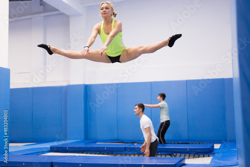 Young sporty woman with friends practicing and jumping in trampoline center
