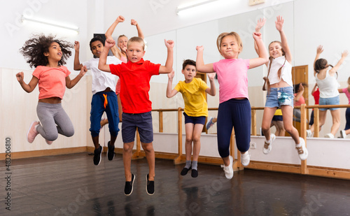 Group of cheerful tweens jumping with female trainer during modern dances class..