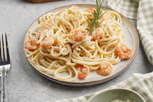 Flat plate with pasta spaghetti with heavy cream and roasted shrimps with garlic sauce and parmesan cheese on grey concrete surface