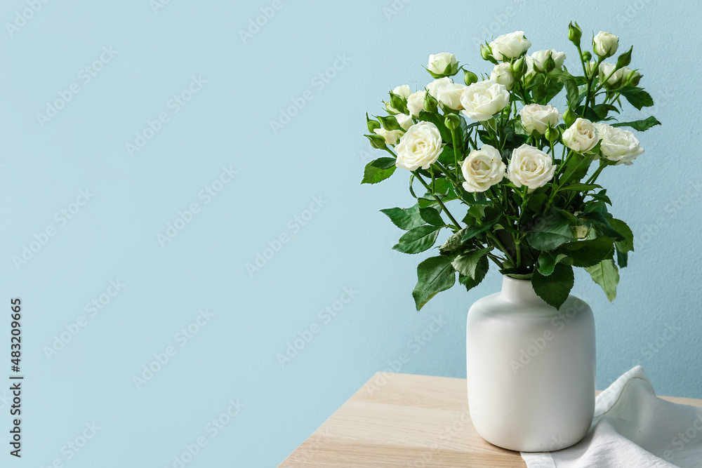 Vase with bouquet of beautiful roses on table near blue wall Vase with bouquet of beautiful roses on table near blue wall