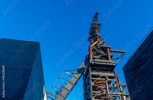 A low angle shot of a reconverted steel chimney tower and modern buildings photo
