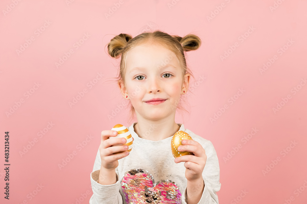 Funny little blonde girl smiling and playing with golden easter eggs on pink background. Happy Easter concept Funny little blonde girl smiling and playing with golden easter eggs on pink background. Happy Easter concept