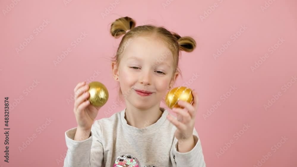 Funny little blonde girl smiling and playing with golden easter eggs on pink background. Happy Easter concept Funny little blonde girl smiling and playing with golden easter eggs on pink background. Happy Easter concept