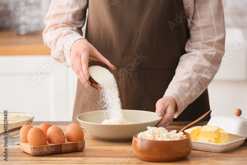 Fotografija Woman adding sugar into bowl with cottage cheese for preparing pancakes at kitch