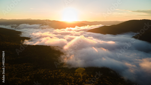 Aerial view of bright foggy morning over dark mountain forest trees at autumn sunrise. Beautiful scenery of wild woodland at dawn © bilanol