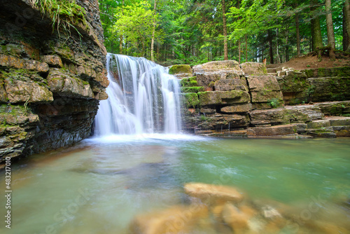 Waterfall on mountain river with white foamy water falling down from rocky formation in summer forest