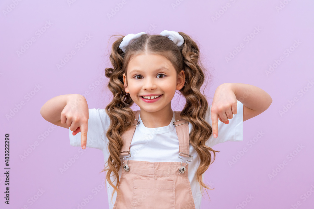 The child points down at the advertisement and smiles. A children with curly hair on an isolated background. The child points down at the advertisement and smiles. A children with curly hair on an isolated background.