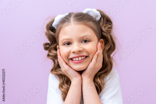 Portrait of a small beautiful smiling girl on a purple background with curly hair.