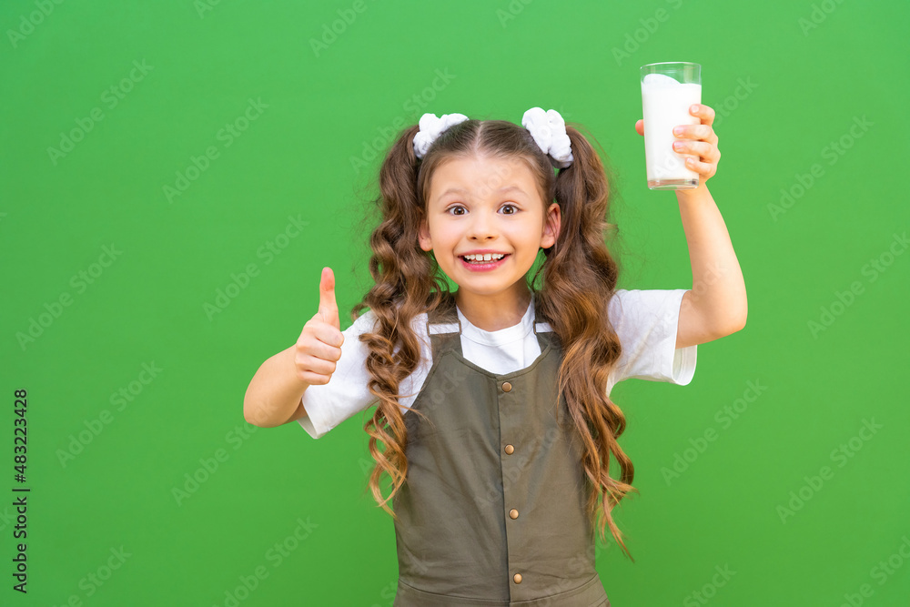 A glass of fresh milk in the hands of a beautiful girl, the child holds a glass of kefir and shows a thumb to the top. A glass of fresh milk in the hands of a beautiful girl, the child holds a glass of kefir and shows a thumb to the top.