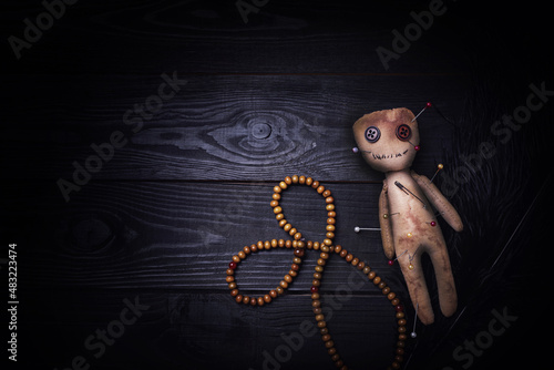 Voodoo doll pierced with pins, beads and feather on black wooden table, flat lay photo