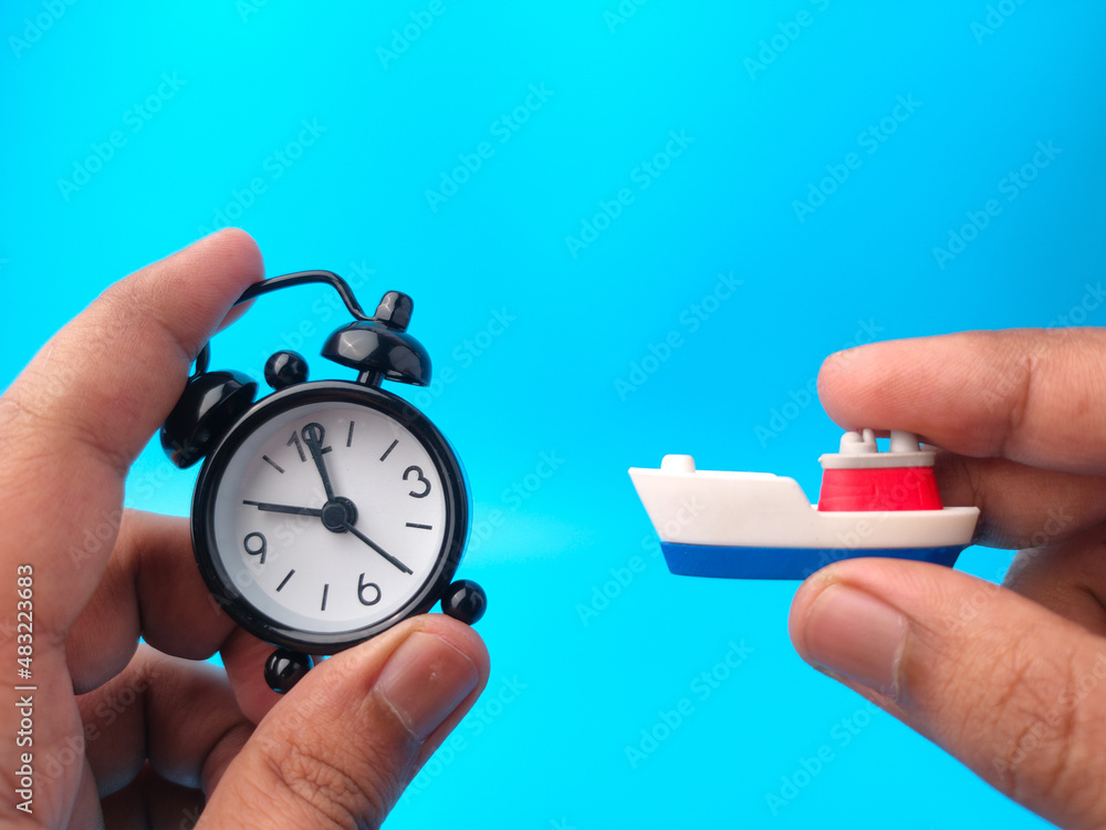 Hand holding clock and toy ships on blue background. Travel concept.