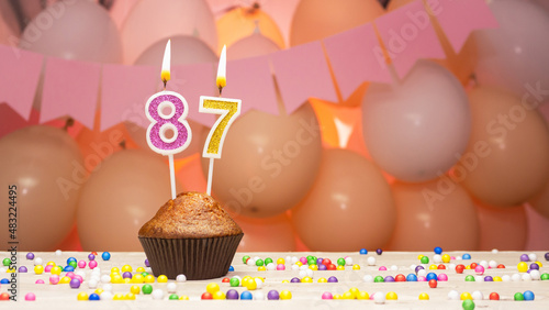 Decorations with balloons and a happy birthday candle with the number 87 for a woman. Happy birthday greetings in pink flowers for eighty-seven years old for an elderly woman, copy space. Muffin photo